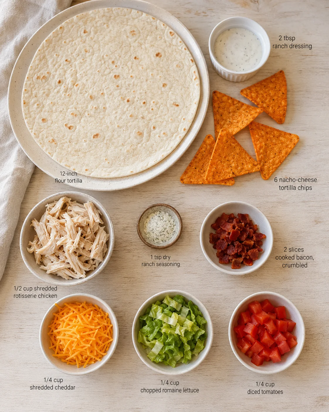 Top-down view of a large flour tortilla with bowls of shredded chicken, cheese, lettuce, tomatoes, and bacon.