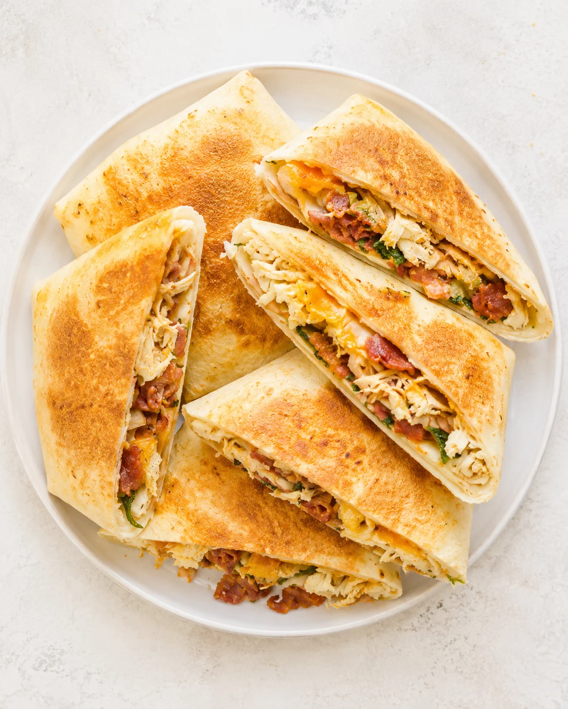 Golden-brown quesadillas filled with chicken, cheese, and herbs on a white plate.